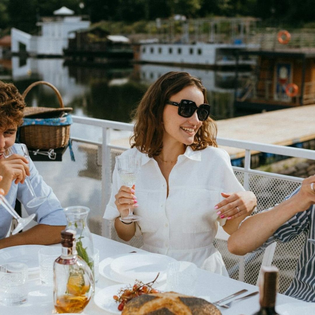 Group of friends enjoying drinks and laughter at a summer outdoor gathering by the water.